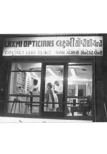 The black-and-white sign for ’laxmi opticians’ with bilingual text in english and gujarati, advertising a contact lens clinic.