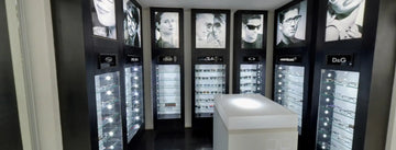 Black-framed eyewear display cases with illuminated glass fronts showcasing various designer sunglasses and prescription glasses from brands like ray-ban, oakley, montblanc, and d&g.
