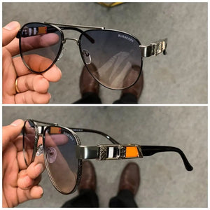 Burberry aviator sunglasses with gradient gray lenses and a metallic frame featuring an orange, black, and silver accent on the temple.