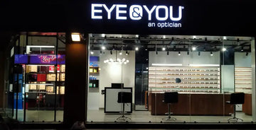 The illuminated ’eye & you an optician’ sign above the storefront features bold, white led lettering against a dark background.