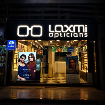 Laxmi opticians storefront with illuminated white logo and glass windows displaying eyewear advertisements.